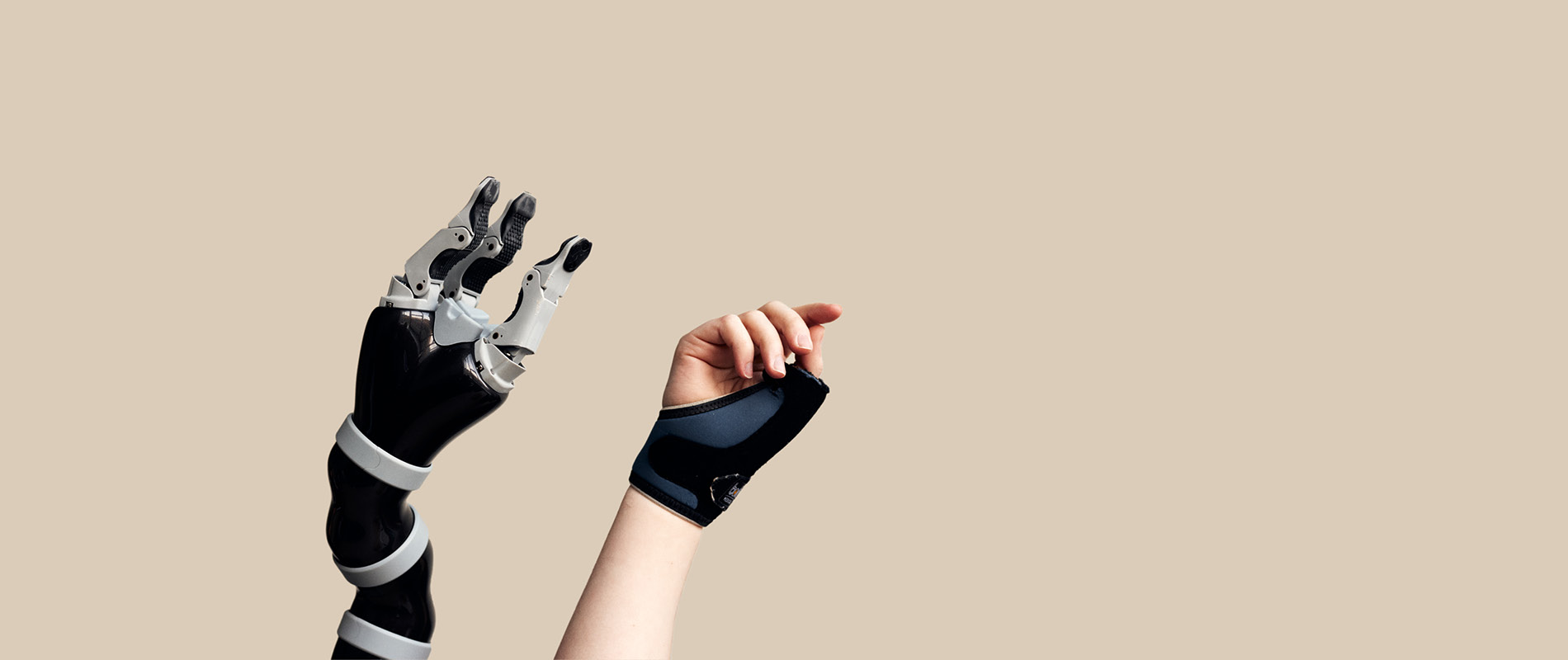 Eine Roboterhand wird neben einer menschlichen Hand vor einem sandfarbenen Hintergrund in die Luft gestreckt