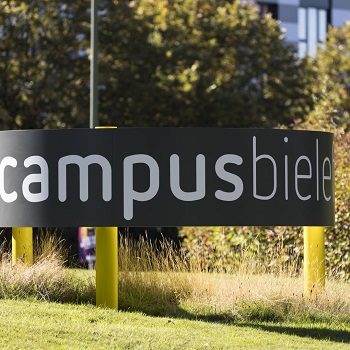 Sign with Campus Bielefeld lettering on a meadow