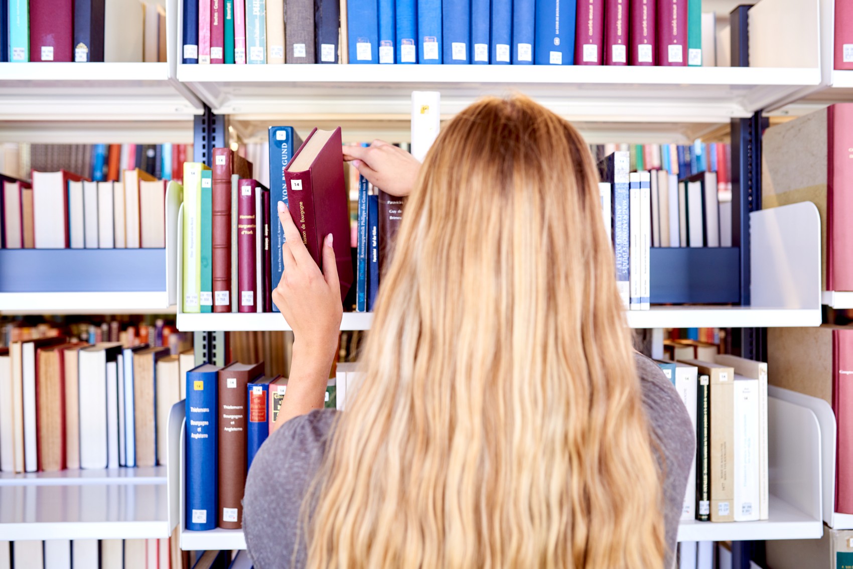 Studierende nimmt ein Buch aus einem Bücherregal
